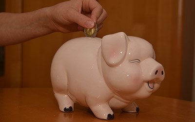 Zwei Euro werden in ein Sparschwein geschmissen.